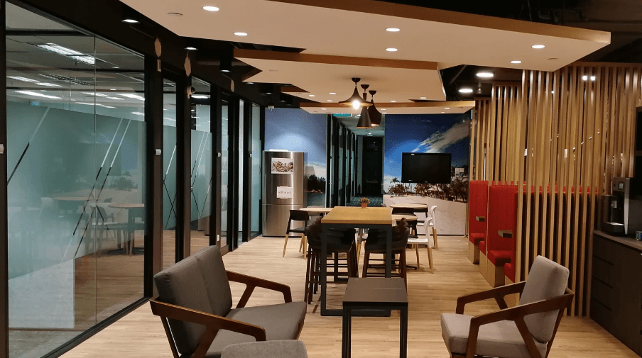 Cozy office break area with modern furniture, wooden flooring, glass walls, and warm ambient lighting