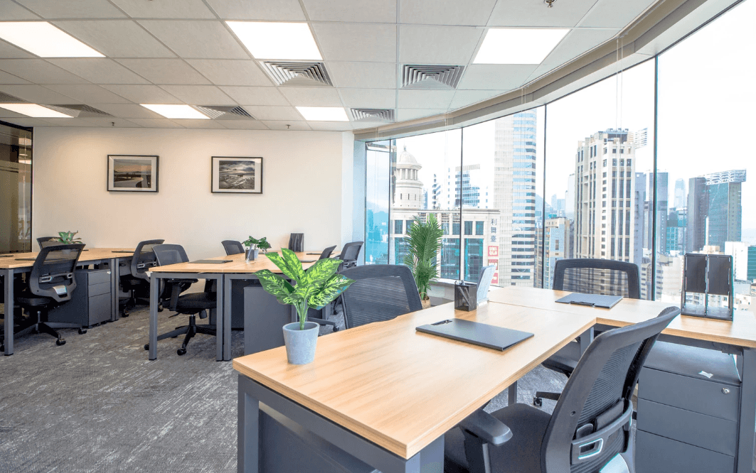 Modern office space with desks, ergonomic chairs, and panoramic city views through floor-to-ceiling windows.