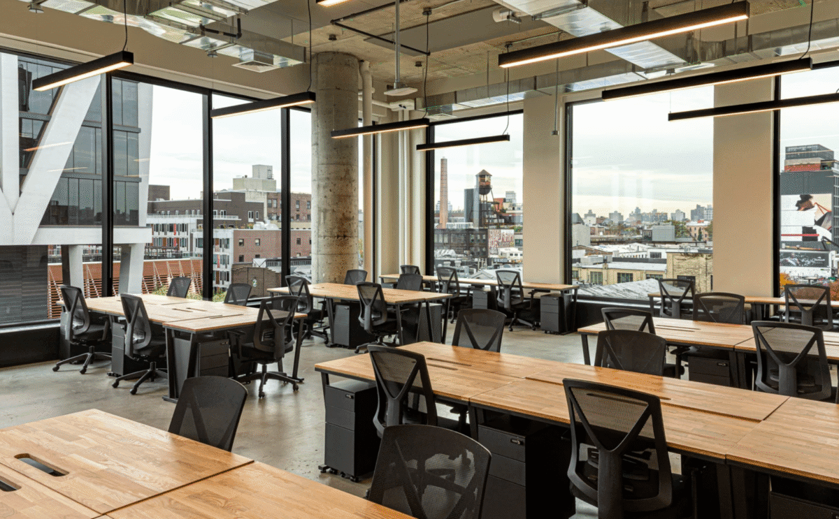 Modern open-concept coworking office with large windows, wood desks, and panoramic city views.
